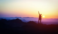 Man silhouette stand on peak of moutain with hand up. Success and motivation. Mountains landscape with sunset as perfect driven leadership concept stock photo