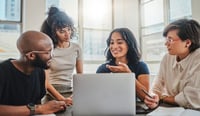 Four diverse enthusiastic employees sitting around a laptop in an office considering AI as employee trust in the AI revolution concept 