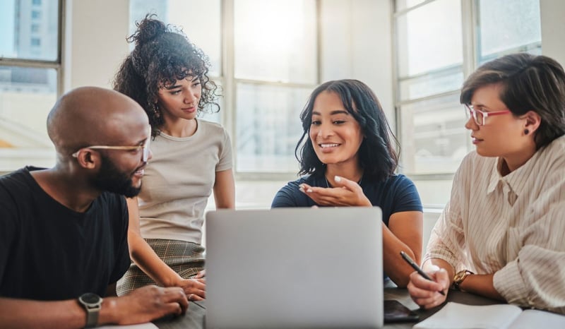 Image for Four diverse enthusiastic employees sitting around a laptop in an office considering AI as employee trust in the AI revolution concept 