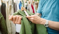 Man looking at a resale item on a hanger off a rack in a fashion store.