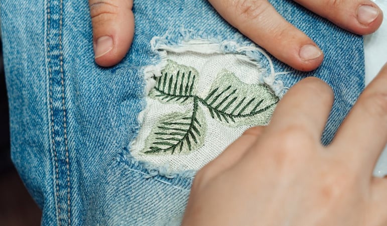 A woman mends jeans, sews a patch on a hole, hands close-up.Mending clothes concept,reusing old jeans stock photo