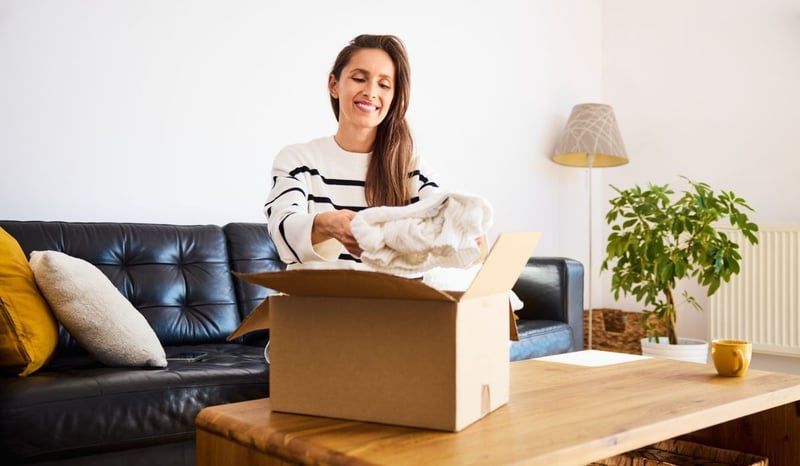 Image for Smiling woman packing preloved clothes for resale, embracing sustainable fashionindoor, cheerful stock photo