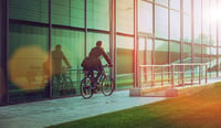 Man member of c-suite riding bicycle beside modern office building stock photo as business case for sustainability concept