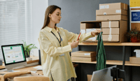 Side view of young woman with smartphone taking photo of shirt on hangers stock photo