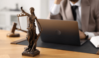 Lawyer working with laptop utilising GenAI at table in law firm office, focus on statue of Lady Justice stock photo