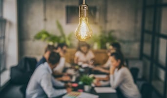 Creativity at work concept with lightbulb illuminating the image over a desk full of workers stock photo