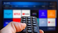 A man is holding a remote control of a smart TV in his hand. In the background you can see the television screen with streaming entertainment apps for video on demand stock photo