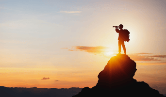 Silhouette of man holding binoculars on mountain peak against bright sunlight sky background  stock photo