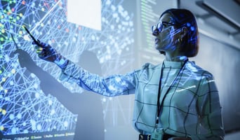 Young Female Teacher Giving a Data Science Presentation in a Dark Auditorium with Projecting Slideshow with Artificial Intelligence Neural Network Architecture. Taking a people first approach to AI implementationConcept stock photo