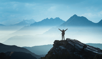 Positive man celebrating success on top of mountain after deciding to make purpose-driven change