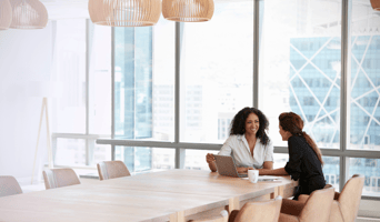 Two women in a boardroom using laptop to unlock business potential through purpose in a meeting